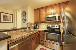 A modern kitchen with wooden cabinets, stainless steel appliances, a tiled backsplash, and a dishwasher. - One Bedroom Unit With Beautiful Ocean Views From Balcony! (Oceanside)