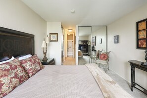 A bedroom with a large bed, a bedside table with a lamp, a mirror, and a dresser. - One Bedroom Unit With Beautiful Ocean Views From Balcony! (Oceanside)