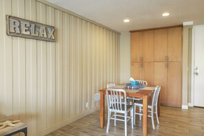 Uma sala de jantar com uma mesa de madeira, cadeiras brancas e um letreiro 'RELAX' na parede.