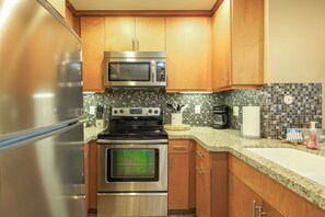 A kitchen with stainless steel appliances, wooden cabinets, and a tiled backsplash. - Saphire Sands (Oceanside)