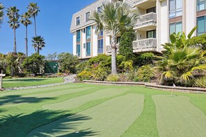 A golf course with a well-maintained green, surrounded by palm trees and a multi-story building with balconies. - Enjoy Breathtaking 1br/1ba With Stunning Views of the Pool and Ocean (Oceanside)