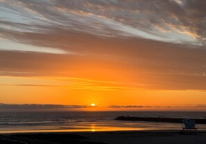 A beach scene with a sunset, a lifeguard stand, and a distant shoreline. - Enjoy Breathtaking 1br/1ba With Stunning Views of the Pool and Ocean (Oceanside)