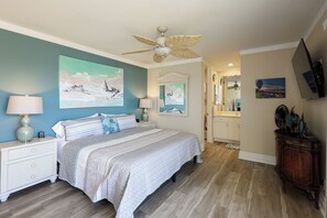 Ein Schlafzimmer mit Bett, Nachttischen, Deckenventilator, Kunstwerken, Fernseher und einem Holzschrank.