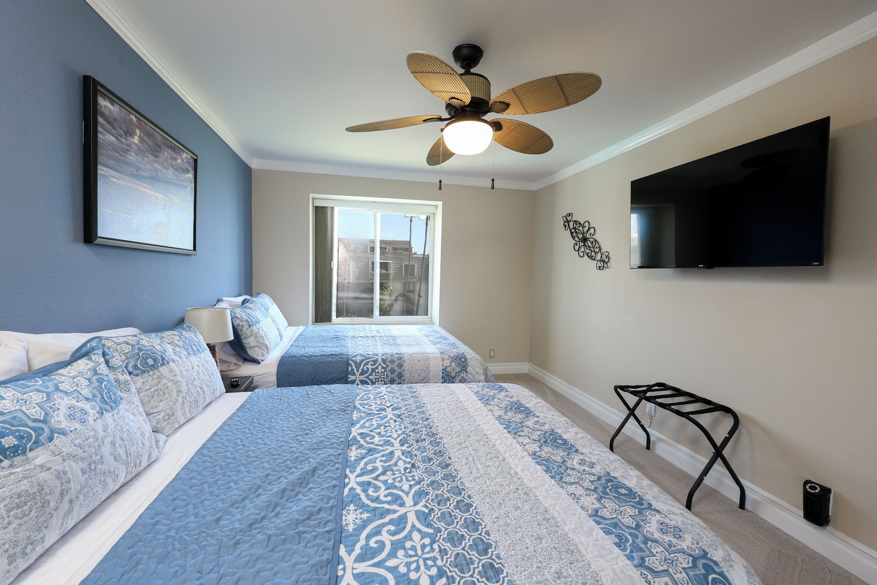 A bedroom with two beds, a ceiling fan, a TV, and a window.