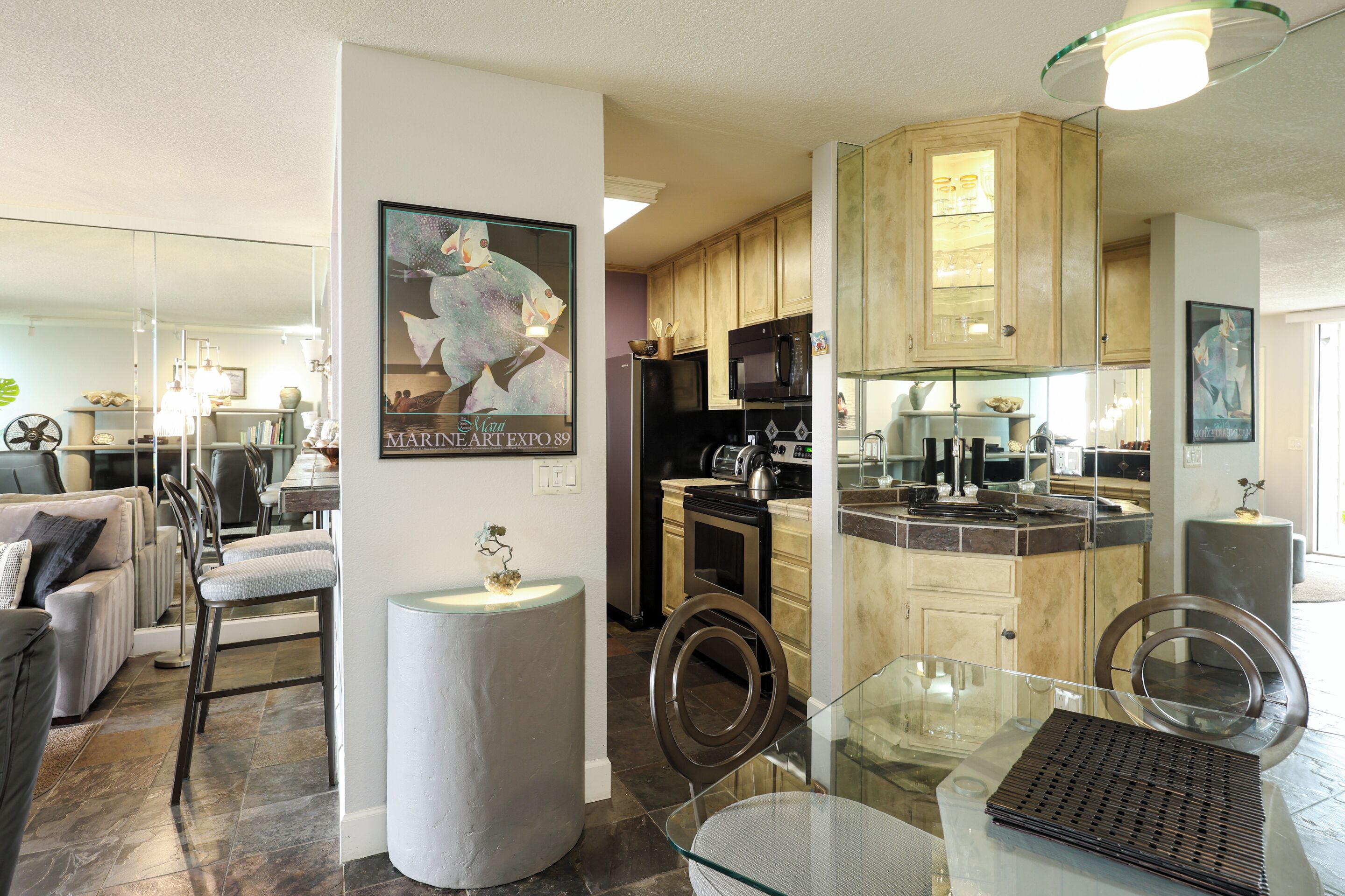 A modern kitchen with wooden cabinets, a glass dining table, and a poster on the wall.