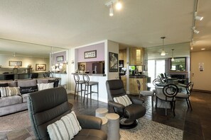 A modern living room with a sofa, chairs, a dining area, kitchen, and a large mirror. - Coastal Escape (Oceanside)
