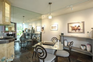 A modern kitchen with a glass dining table, chairs, and a hanging light fixture. - Coastal Escape (Oceanside)