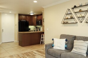 A kitchen with a refrigerator, microwave, and island. There is a gray couch with striped pillows and a white pillow with tassels. - Tropical Beach 1br/1ba Retreat at North Coast Village (Oceanside)