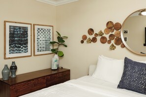 A bedroom with a bed, a dresser, a mirror, and wall decorations including framed artworks and wooden circles. - Tropical Beach 1br/1ba Retreat at North Coast Village (Oceanside)