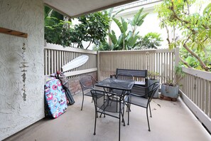 A patio with a table and chairs, a surfboard, and potted plants. - Tropical Beach Retreat (Oceanside)