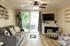 A living room with a sofa, armchairs, a fireplace, a television, and a ceiling fan. - Tropical Beach Retreat (Oceanside)