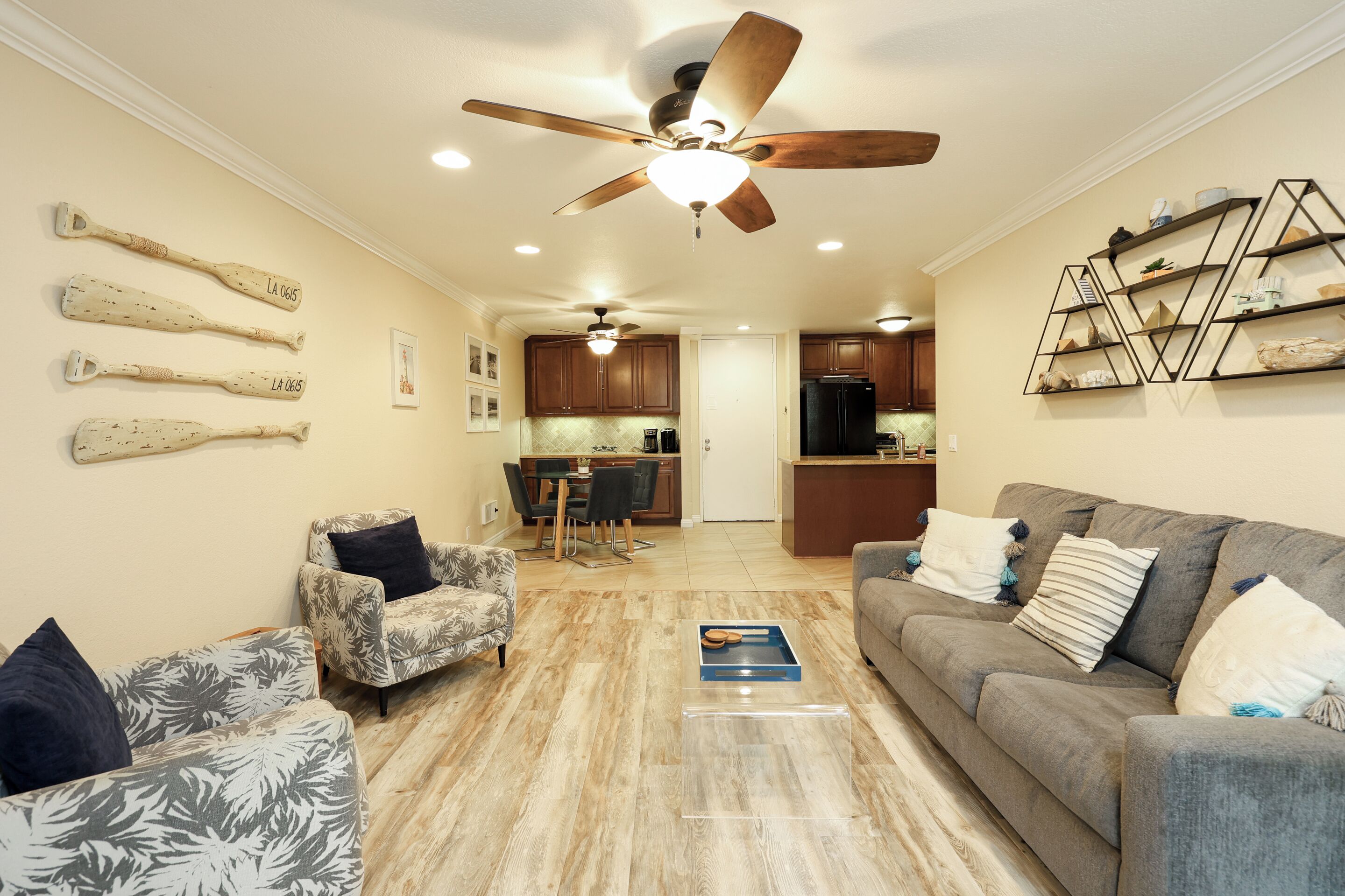 A living room with a ceiling fan, a sofa, a coffee table, and a dining area with chairs and a kitchen in the background.