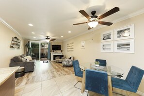 A spacious living area with a dining table, blue chairs, a ceiling fan, and a fireplace. - Tropical Beach Retreat (Oceanside)
