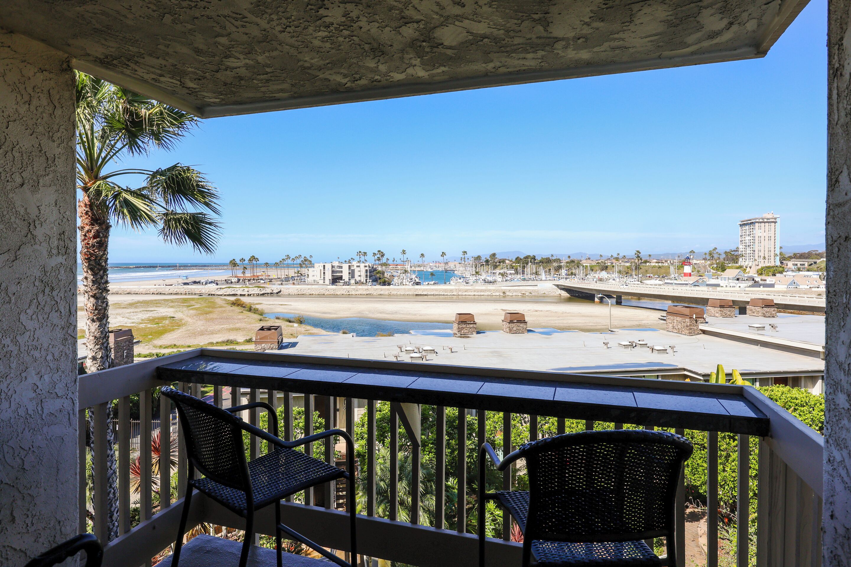Ein Balkon mit zwei Stühlen, Blick auf den Strand und ein hohes Gebäude in der Ferne.