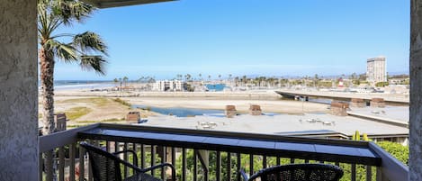 A balcony with two chairs, a view of the beach, and a tall building in the distance.