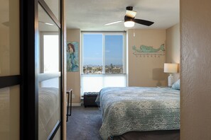 A bedroom with a bed, a ceiling fan, a window with a view, and a wall with a painting. - Harbor and Ocean View Coastal Retreat Walk to Beach & Marina (Oceanside)