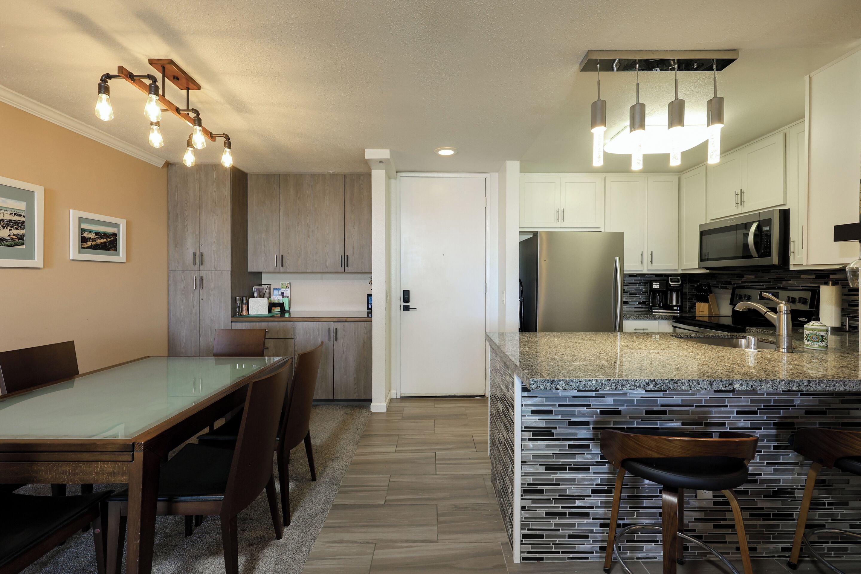 A modern kitchen with granite countertops, stainless steel appliances, and a dining area with a glass-top table and wooden chairs.