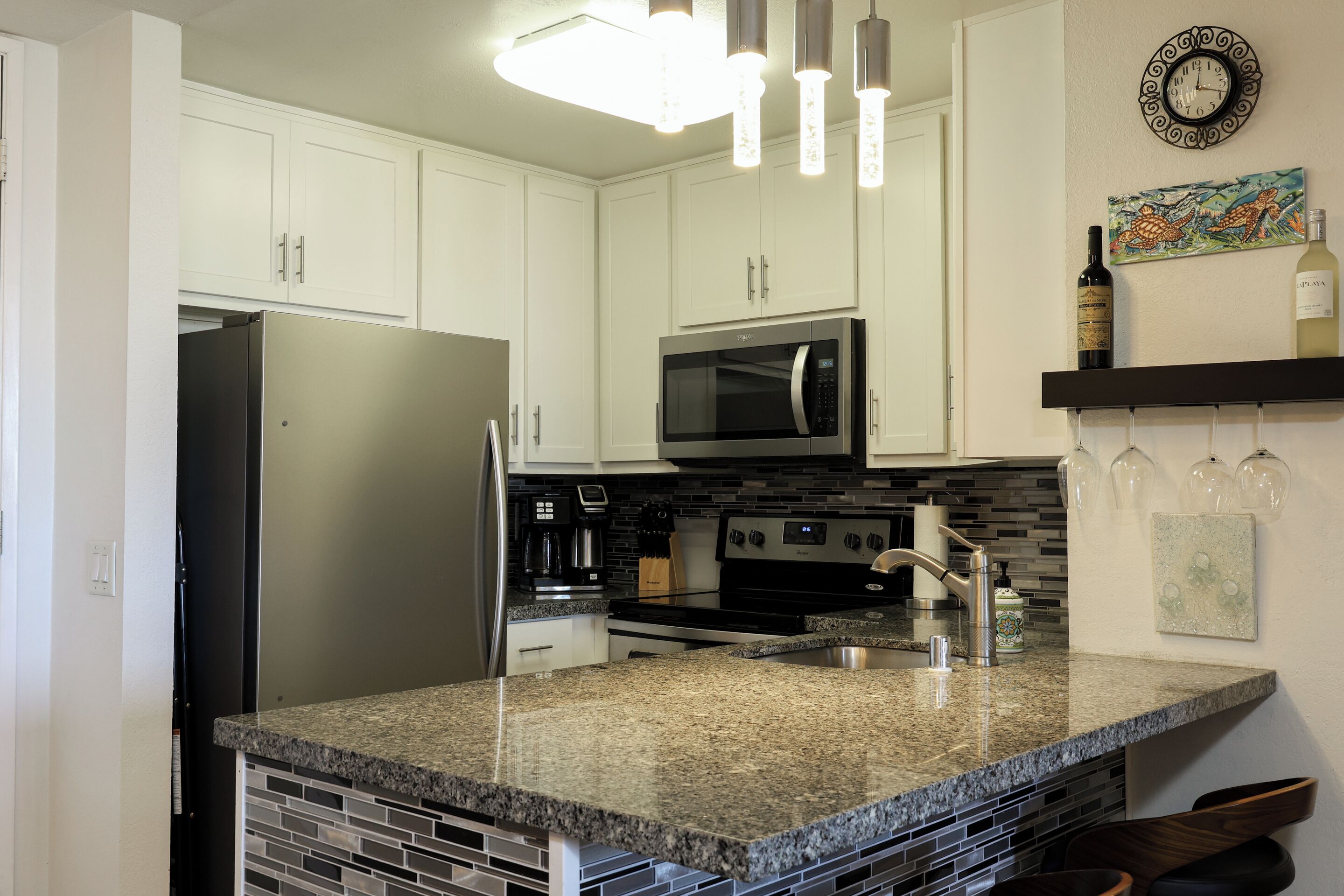 A kitchen with white cabinets, a stainless steel refrigerator, a microwave, a stove, and a sink.