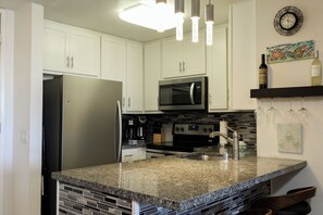 A kitchen with white cabinets, a stainless steel refrigerator, a microwave, a stove, and a sink. - Harbor Horizon Retreat (Oceanside)