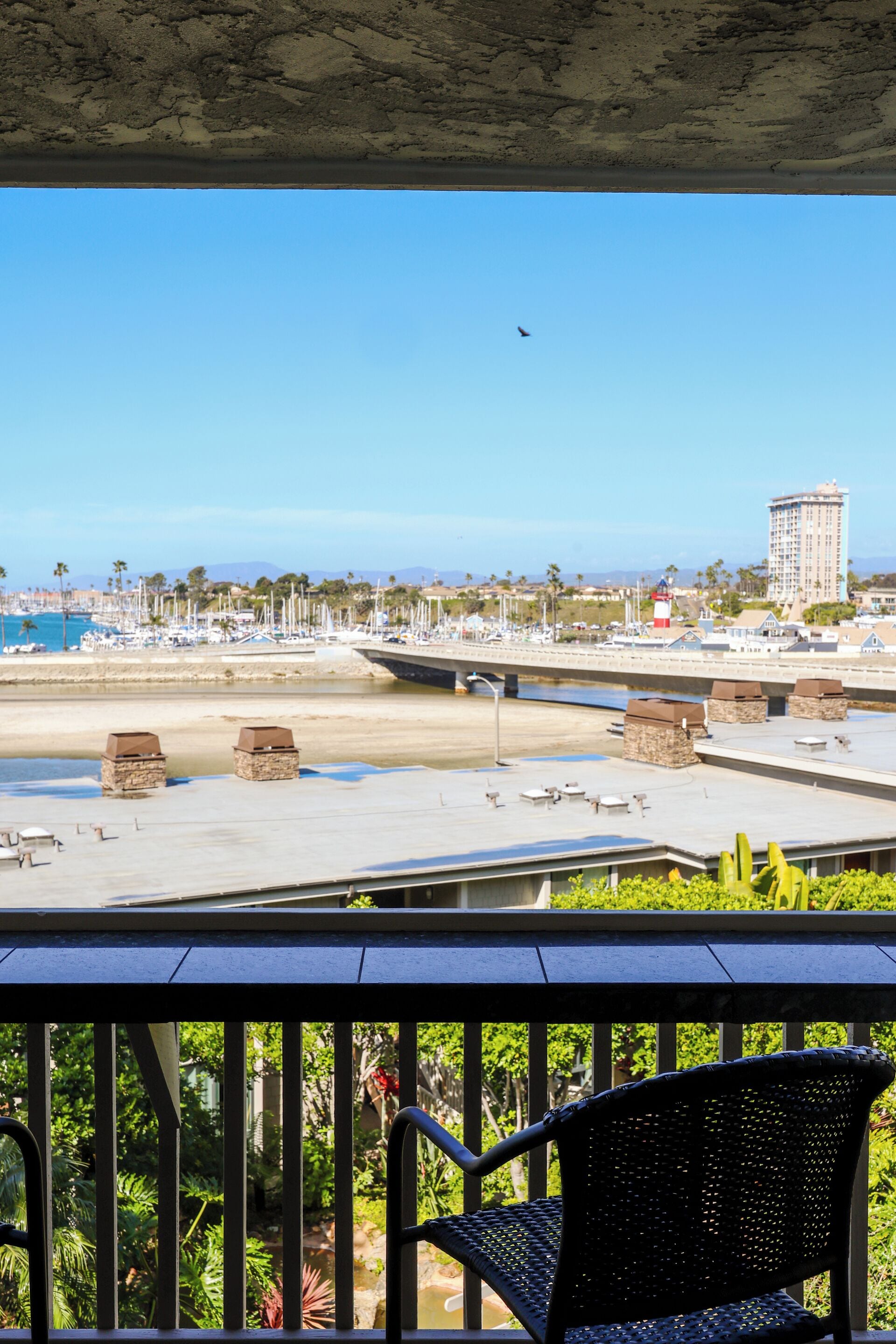 Un balcón con vista a una playa, una silla y un edificio a lo lejos.