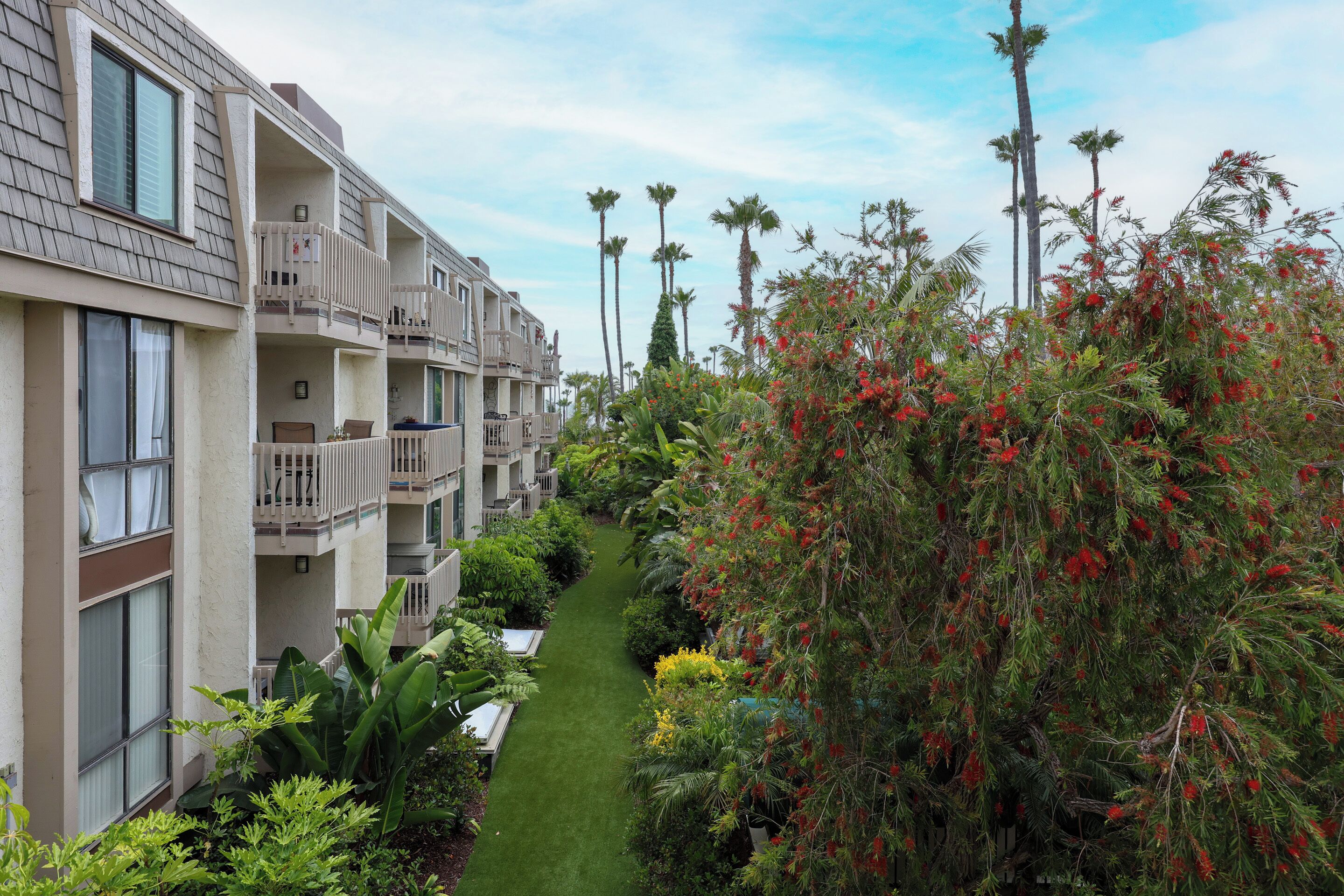 Ein mehrstöckiges Hotel mit Balkonen, einem gepflegten Garten und hohen Palmen.