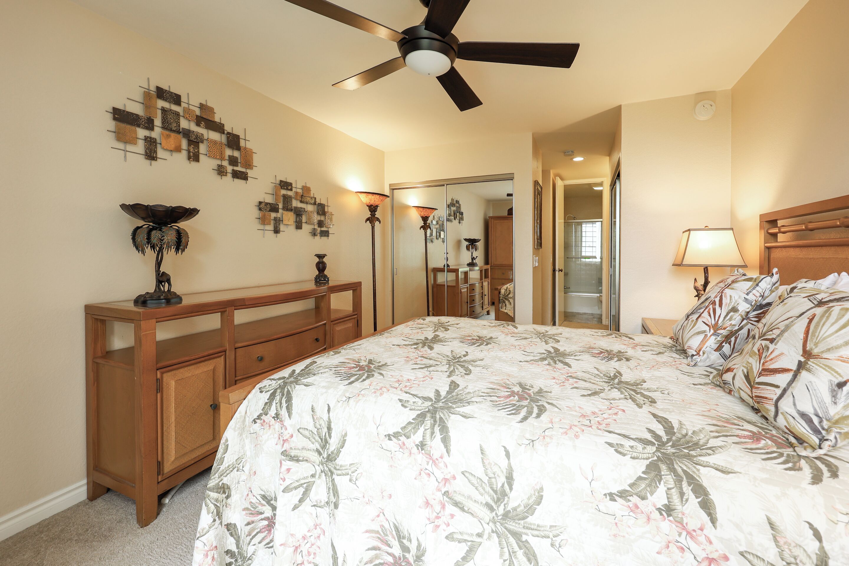 A bedroom with a bed, a ceiling fan, a wooden dresser, and a mirror.