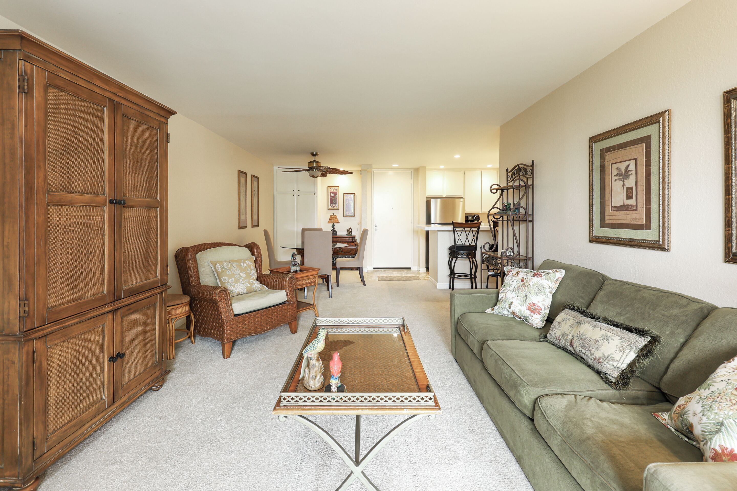 A spacious living room with a green sofa, wicker armchairs, a coffee table, and a large wooden cabinet.