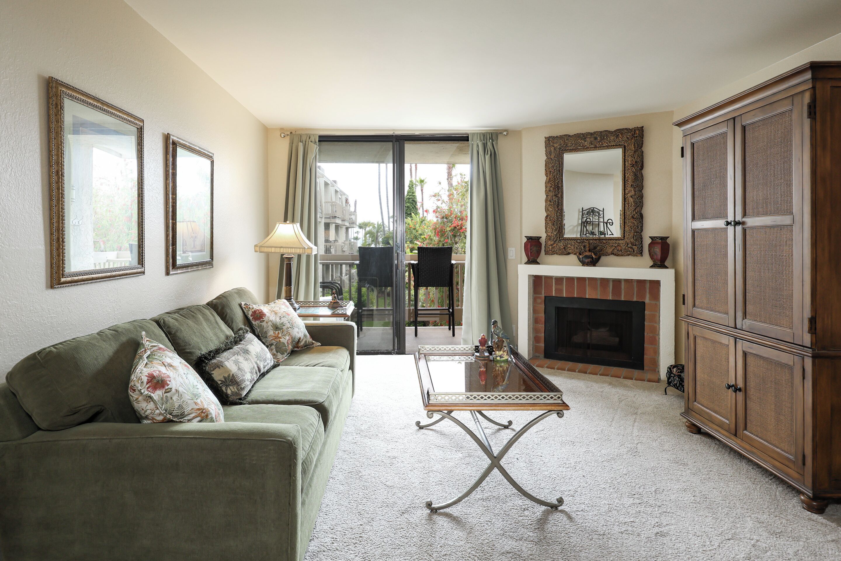 A living room with a green sofa, a glass-top coffee table, a fireplace, and a large mirror.