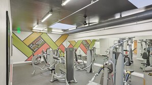 A gym with various exercise machines, a large mirror, and a colorful wall design. - Enjoy Beautiful Views in This New One Bedroom Unit (Oceanside)