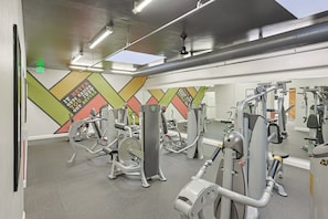 A gym with various exercise machines, a large mirror, and a colorful wall design. - Enjoy Beautiful Views in This New One Bedroom Unit (Oceanside)
