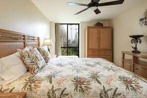 A bedroom with a bed, a ceiling fan, a window with a view of palm trees, and a wooden cabinet. - Enjoy Beautiful Views in This New One Bedroom Unit (Oceanside)