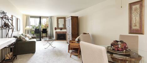 A spacious living room with a fireplace, a dining area with a glass table, and a ceiling fan.