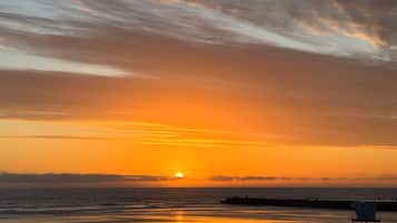 Une scène de plage avec un coucher de soleil, un poste de surveillance des sauveteurs et une côte lointaine.