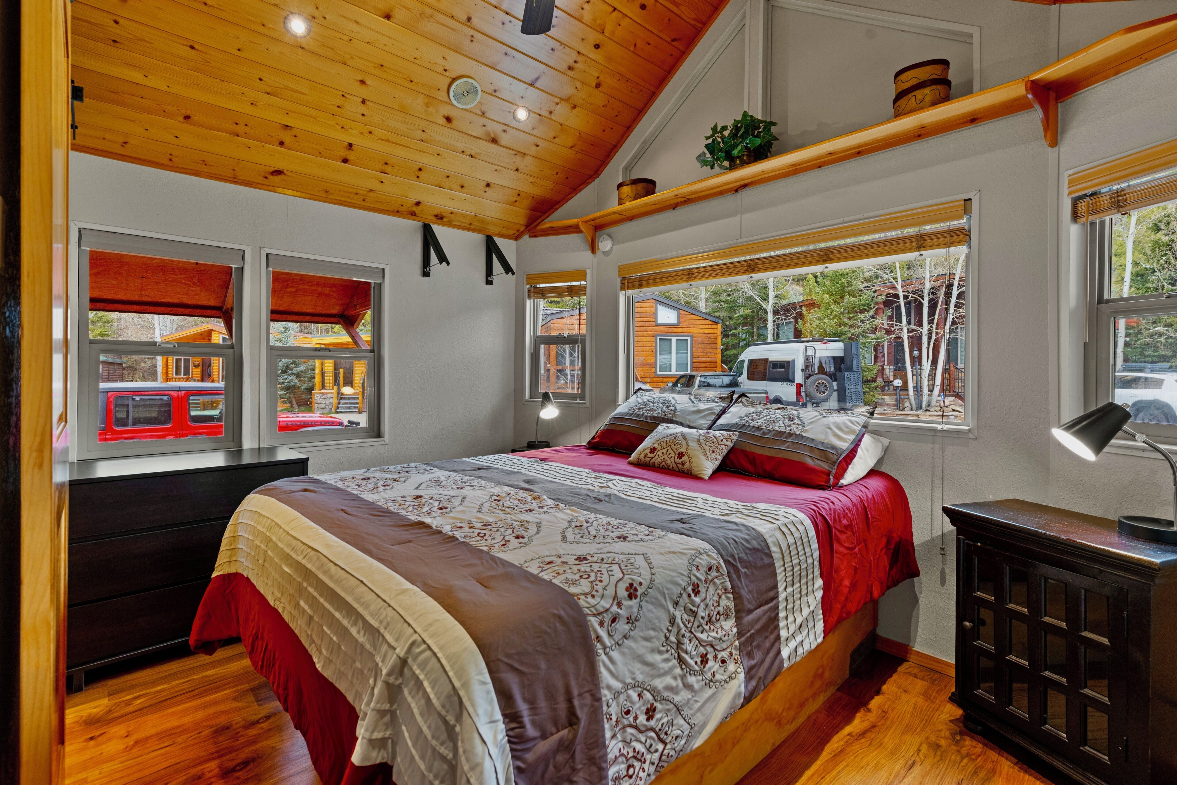 A bedroom with a large bed, wooden ceiling, and a window with a view of a vehicle and buildings outside.