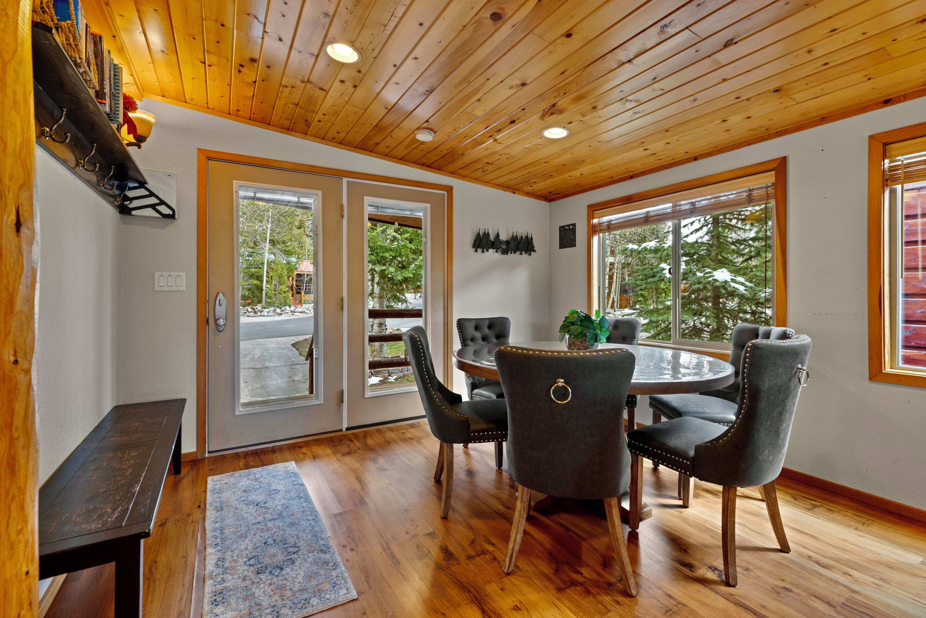A room with a wooden ceiling, a round dining table with chairs, a bench, and a rug.