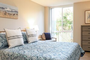 Ein Schlafzimmer mit einem großen Bett, einem Sessel, einer Kommode und einem Fenster mit Blick auf Bäume.