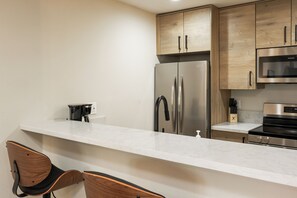 Eine moderne Küche mit einem Edelstahl-Kühlschrank, einer Mikrowelle und einem Herd. Es gibt eine weiße Arbeitsplatte und Holzschränke.