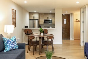 Eine moderne Küche mit Edelstahlgeräten, ein Essbereich mit Holzkohle und einem Tisch, sowie ein Wohnzimmer mit Sofa und Lampe.