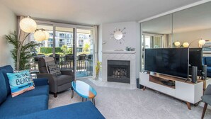 A modern living room with a fireplace, a large flat-screen TV, and a balcony with a view of the city. - Beautiful 2bd/2ba Luxury Cottage Unit With an Oceanview (Oceanside)