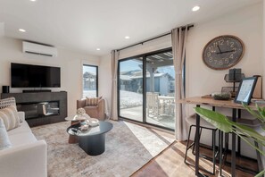 A modern living room with a flat-screen TV, a fireplace, a sofa, a coffee table, and a dining area with a wooden table and chairs. - Romantic Lakefront Condo F5 + Pool - Wapato Chelan (Manson)