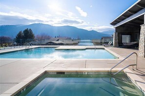 A swimming pool with clear water, surrounded by a stone deck, with mountains in the background. - Romantic Lakefront Condo F5 + Pool - Wapato Chelan (Manson)