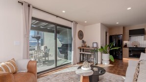 A modern living room with a large sliding glass door leading to a balcony, a dining area with a bar, and a kitchen with a black refrigerator. - Romantic Lakefront Condo F5 + Pool - Wapato Chelan (Manson)