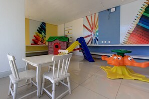 Uma área de recreação infantil com escorrega, estrutura de escalada e mesa com cadeiras.