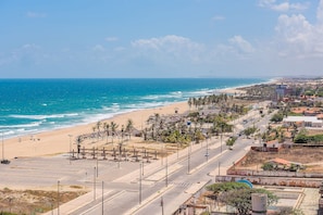 Un paisaje costero con playa, palmeras y una carretera que conduce a un edificio de techo rojo.