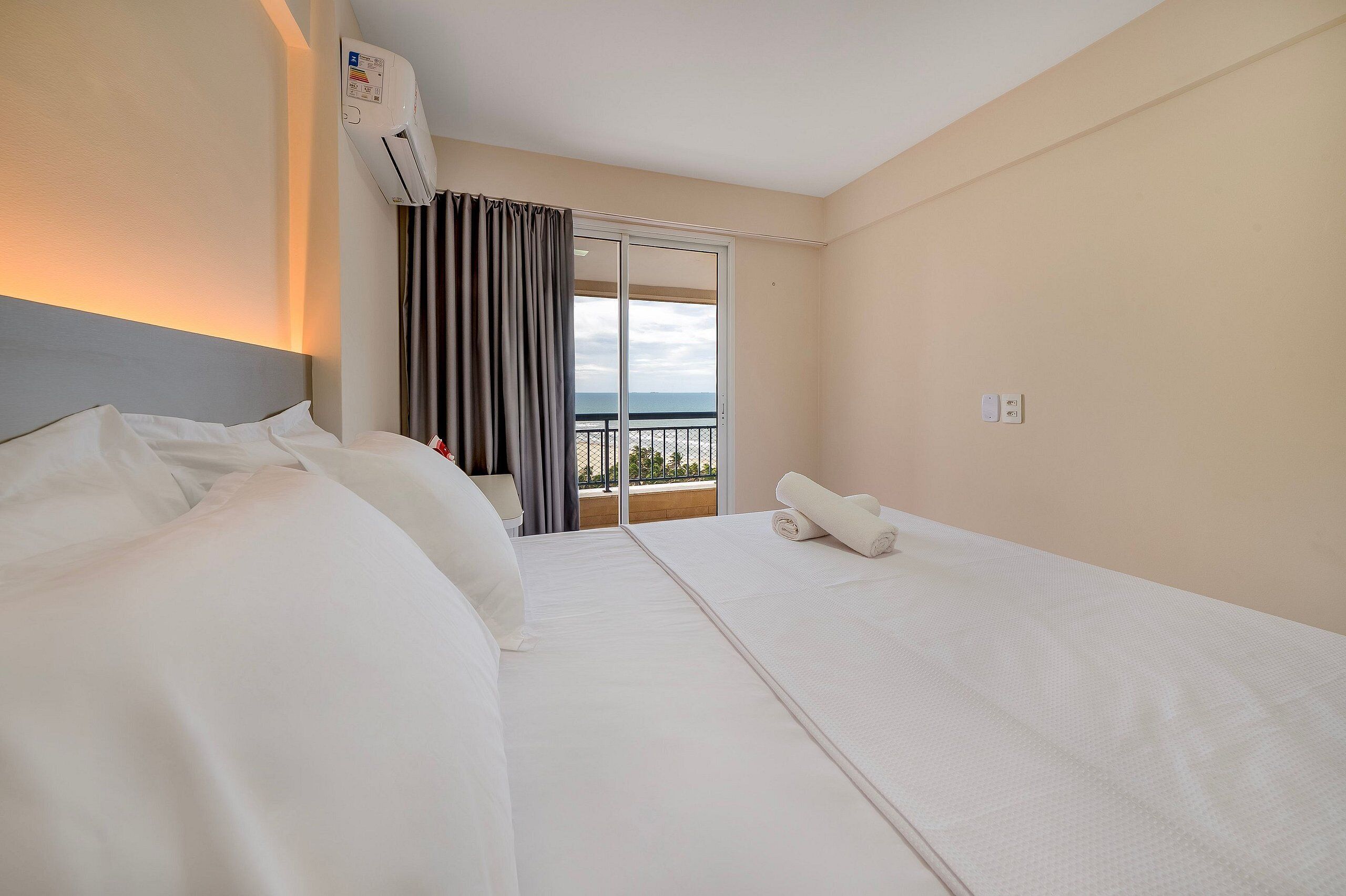 Une chambre d’hôtel avec un lit, une fenêtre avec des rideaux, un appareil de climatisation et une vue sur la mer.