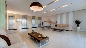 A modern lobby with a sofa, coffee table, and a large potted plant. - Beach Village #1205 - Sea View by Carpediem (Fortaleza)