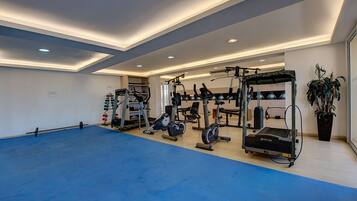 Une salle de sport spacieuse, équipée de divers appareils d’exercice, dotée d’un sol bleu et d’un plafond avec des luminaires encastrés.