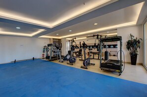 Ett rymligt gym med olika typer av träningsutrustning, ett blått golv och ett tak med infälld belysning.