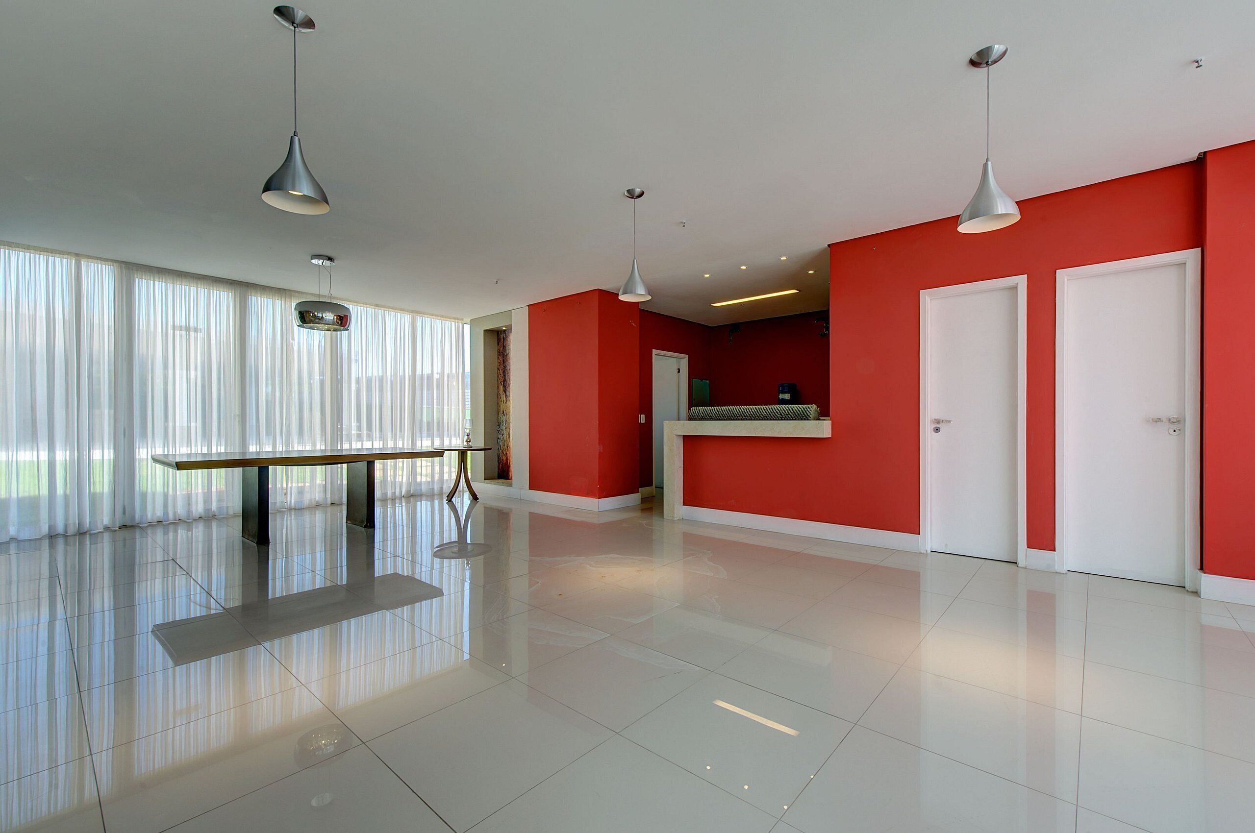 Un hall d’hôtel spacieux et moderne, agrémenté d’un mur d’accent rouge, d’un comptoir d’accueil et d’une grande fenêtre ornée de rideaux légers.