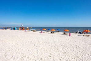A beach with sun loungers and umbrellas, a lifeguard station, and the ocean in the background. - NEW! Beachfront Condo! 2 MasterSuites! Gulf Views! (Long Beach)